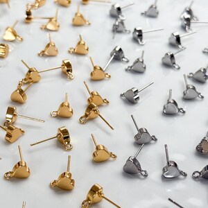Op de afbeelding: Een verzameling hartvormige oorstekers met oogjes voor het maken van sieraden. De set bevat zowel goudkleurige als zilverkleurige metalen onderdelen, elk voorzien van een steker en een klein rond oogje aan de onderkant van het hart.