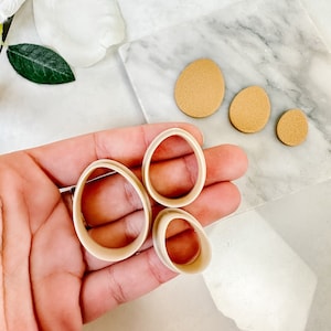 May include: Four beige oval-shaped cookie cutters of different sizes, held in a hand.