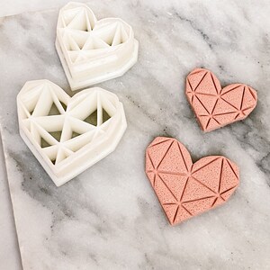 Può includere: Due tagliabiscotti a forma di cuore bianchi con un design geometrico e due biscotti a forma di cuore rosa con un design geometrico.