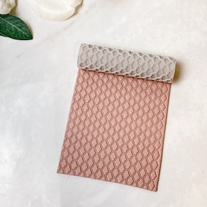 Può includere: Un mattarello in silicone rosa e grigio con un motivo geometrico. Il mattarello è steso su una superficie bianca.