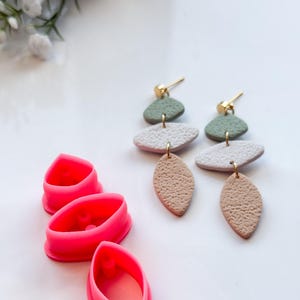 May include: Pink silicone mold for making three different sized teardrop shaped earrings. The mold is shown next to a pair of earrings made with the mold.