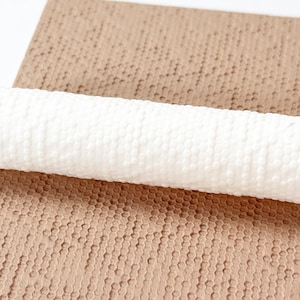 May include: A white, textured rolling pin rests on a brown, honeycomb-patterned surface. The rolling pin has a cylindrical shape with a repeating pattern of small, raised dots. The brown surface has a similar pattern.