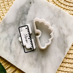 May include: White plastic cookie cutter shaped like a cloud with a scalloped edge. A ruler is included for size reference, measuring 9.5 cm.