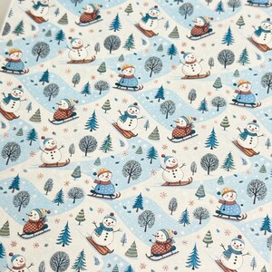 May include: A repeating pattern featuring snowmen on skis and sleds, set against a light blue and white winter landscape. The snowmen wear hats, scarves, and coats in various colours. Trees and snowflakes complete the winter scene.