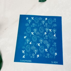Könnte beinhalten: Blaue Nagelkunst-Schablone mit weißen Umrissen von Figuren, Blumen und Sternen. Die Schablone trägt den Text "Luxymolds" und "S-404".