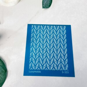 May include: Blue plastic stencil with a white geometric pattern. The stencil has the text "Luxymolds" and "S-333" printed on it.
