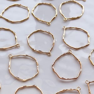 Peut inclure: Plusieurs cadres en métal doré de formes irrégulières avec de petites boucles, destinés à la création de bijoux. Disposés sur une surface blanche, ils mettent en valeur leurs formes organiques variées et leurs surfaces réfléchissantes.