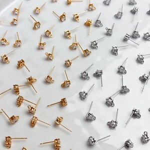 May include: A collection of gold-tone and silver-tone stud earring findings, each featuring a single clear round cubic zirconia stone set in a metal prong setting with a small loop at the base for attaching additional jewellery components.