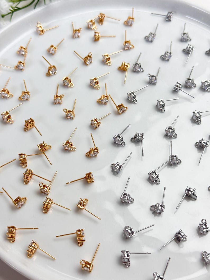 May include: A collection of gold-tone and silver-tone stud earring findings, each featuring a single clear round cubic zirconia stone set in a metal prong setting with a small loop at the base for attaching additional jewellery components.