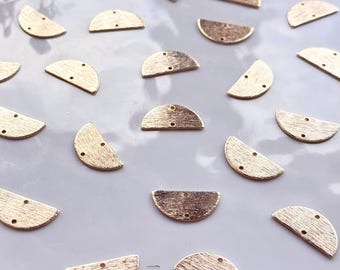 May include: A selection of gold-coloured, semi-circular metal jewellery components. Each piece has a textured surface and two or three small holes for attachment. The components are scattered on a light grey surface.