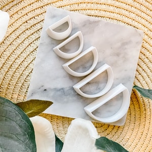 May include: Set of five white plastic half-circle cookie cutters of varying sizes, arranged in a descending order of size on a white marble surface.