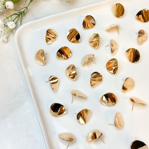 Peut inclure: Une collection de boucles d'oreilles rondes et ondul&eacute;es dor&eacute;es sur une assiette blanche. Les boucles d'oreilles sont toutes de la m&ecirc;me forme et de la m&ecirc;me taille, et elles sont dispos&eacute;es de mani&egrave;re al&eacute;atoire.