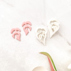 May include: Two pink and two white plastic leaf-shaped cookie cutters on a white marble surface.
