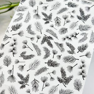 May include: A sheet of white paper with black outlines of various pine branches and needles. The design is a repeating pattern.