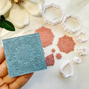 Peut inclure: Une main tient un carré turquoise orné d'un motif mandala complexe. Divers tampons mandala corail et des emporte-pièces blancs sont disposés autour, suggérant un thème artisanal ou de pâtisserie.