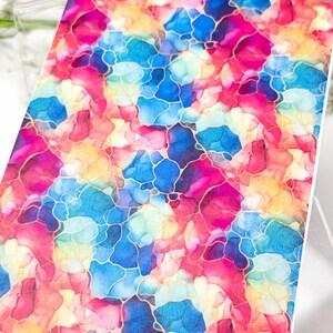 May include: A colorful abstract design featuring a blend of pink, blue, yellow, and orange hues. The design has a watercolor effect with gold-colored outlines, creating a vibrant and artistic look. The design is on a rectangular surface.