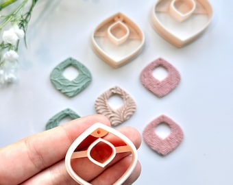 Peut inclure: Ensemble de composants et de découpoirs pour boucles d'oreilles en pâte polymère. Les découpoirs sont roses clair, en forme de goutte géométrique avec un centre carré. Les boucles d'oreilles finies sont vertes, roses et beiges, avec des motifs texturés.