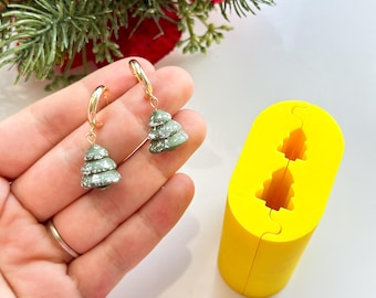 May include: A pair of gold hoop earrings with green and white Christmas tree charms. A yellow silicone mold with a Christmas tree design is also shown.