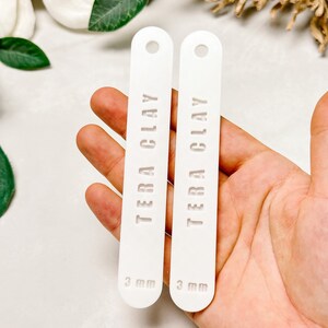 May include: Two white rectangular clay tags with rounded edges and a hole at the top. The tags are labelled "TERA CLAY" and "3 mm".
