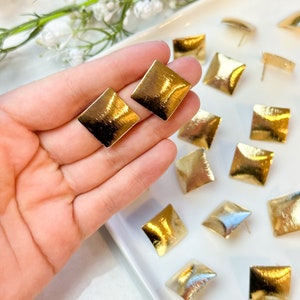 May include: A set of gold square-shaped earrings with a brushed finish. The earrings are displayed on a white plate.