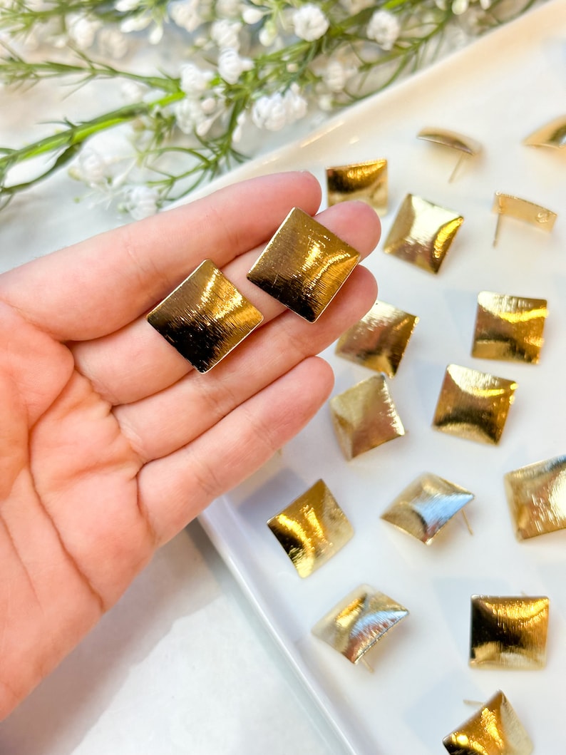 May include: A set of gold square-shaped earrings with a brushed finish. The earrings are displayed on a white plate.