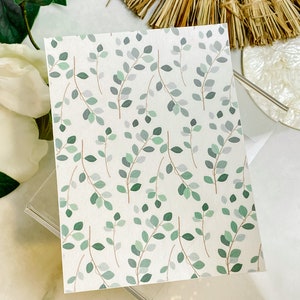 May include: A white card with a repeating pattern of green and gray leaves on a white background.