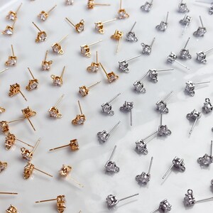May include: A collection of gold-toned and silver-toned stud earring findings, each featuring a single clear cubic zirconia stone set in a prong setting with a small loop at the base for attaching additional jewellery components.