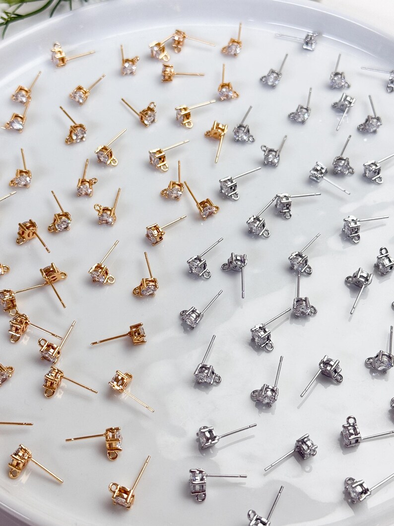 May include: A collection of gold-toned and silver-toned stud earring findings, each featuring a single clear cubic zirconia stone set in a prong setting with a small loop at the base for attaching additional jewellery components.