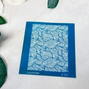 May include: A blue plastic stencil with a white leaf pattern. The stencil is labeled "Luxymolds" and "S-367".