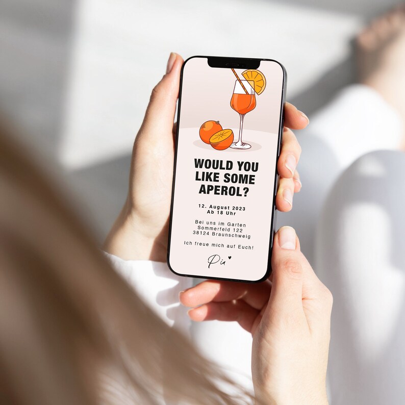 K&ouml;nnte beinhalten: Ein Smartphone-Bildschirm zeigt eine digitale Einladung zu einer Aperol-Party. Die Einladung zeigt eine Comic-Illustration eines Aperol Spritz-Cocktails und den Text "M&ouml;chten Sie etwas Aperol?" Die Einladung enth&auml;lt das Datum, die Uhrzeit und den Ort der Party.