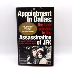 May include: A paperback book titled "Appointment in Dallas: the final solution to the Assassination of JFK." The cover is black with white and red text. A photo of people is at the bottom. The book is a New York Times bestseller.