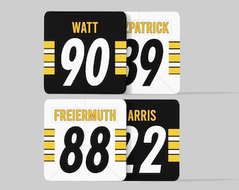 May include: Four black and white square stickers with yellow stripes. The stickers have the names "Watt", "Patrick", "Freiermuth", and "Harris" and the numbers "90", "39", "88", and "22" printed on them.