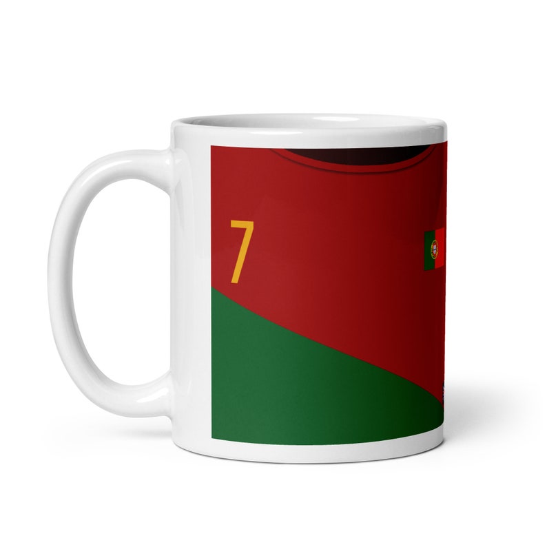 K&ouml;nnte beinhalten: Wei&szlig;e Keramik-Kaffeetasse mit einem rot-gr&uuml;n-gelben Design. Das Design zeigt ein Fu&szlig;balltrikot mit der Nummer 7 und der portugiesischen Flagge.
