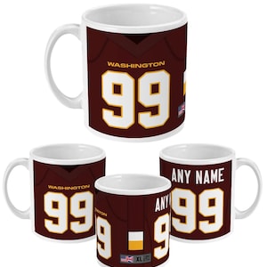 Puede incluir: Taza de café de cerámica blanca con un diseño de camiseta de fútbol marrón y dorada. La camiseta tiene el número "99" y la palabra "WASHINGTON" en ella.