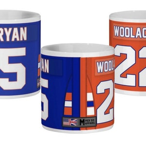 May include: Two white ceramic mugs with a split design featuring a blue and orange hockey jersey. The left mug has the name "RYAN" and the number "5" on the jersey. The right mug has the name "WOOLACOTT" and the number "22" on the jersey.