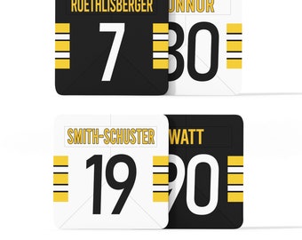 May include: Four white and black rectangular signs with yellow stripes. The signs have names and numbers on them. The names are "Roethlisberger", "Connor", "Smith-Schuster", and "Watt". The numbers are "7", "30", "19", and "90".
