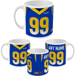 May include: White ceramic coffee mug with a blue and gold design. The mug features a football jersey with the number 99 and the word "RAMS".