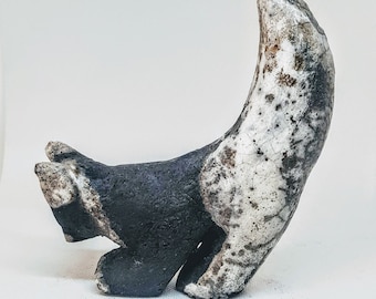 May include: A ceramic sculpture of a stylized animal, possibly a dog or fox, with a black and white speckled glaze. The sculpture is in a playful pose with its tail curled up.