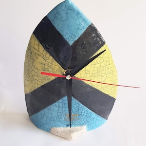 May include: A ceramic clock with a blue, yellow and black geometric design. The clock has a crackle glaze finish and black hands.