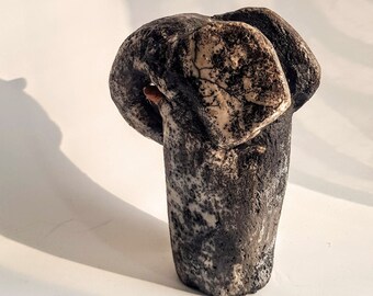 Op de afbeelding: Een zwart-witte keramische sculptuur van een gestileerd menselijk figuur met een rond hoofd en een getextureerd oppervlak.