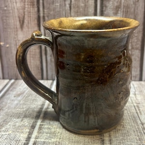 May include: A brown ceramic mug with a handle. The mug has a speckled glaze and a slightly uneven surface.
