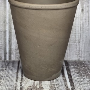 May include: A matte, taupe-colored ceramic cup with a tapered cylindrical shape and a smooth, rounded rim. A metal Westcott ruler is positioned at the base, showing the cup has a diameter of approximately 3.5 inches at the top opening.