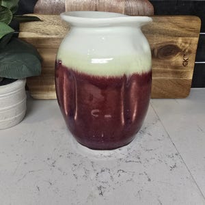 May include: A ceramic pitcher with a white top and a burgundy bottom. The pitcher has a textured surface and a rounded shape.