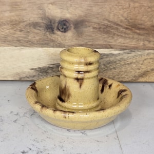 May include: A yellow ceramic candle holder with brown speckles. The holder has a round base and a cylindrical top.