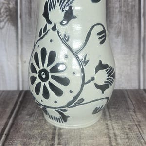 May include: A cream-colored ceramic pitcher featuring dark blue hand-painted floral and circular motifs. A metal Westcott ruler is positioned at the base, showing the pitcher stands approximately 8.5 inches tall with a wide, rounded body shape.