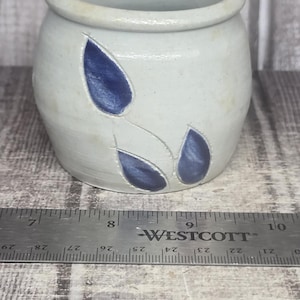 May include: A light gray ceramic pot with a rounded body and a wide opening, featuring three dark blue leaf-shaped indentations on the front. A metal Westcott ruler is positioned in front, showing the pot is approximately 3.5 inches wide.