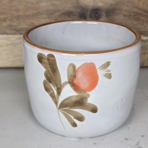 May include: White ceramic bowl with a brown rim and a floral design. The flower is orange with brown leaves and stems. The bowl is round and has a smooth surface.