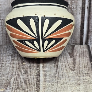 May include: A cream-colored ceramic pot with a black rim and a geometric pattern in black and terracotta. The pot features a row of small holes near the top. A metal ruler is positioned below, showing the pot is approximately 3.5 inches wide.