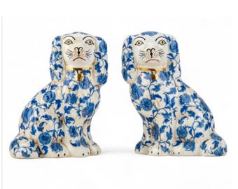May include: Pair of ceramic dog figurines. Each dog is seated with a blue floral pattern on a white background. They have gold collars and detailed facial features. Decorative home decor.