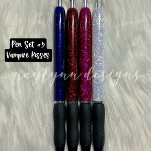 May include: Set of four pens with black barrels and glitter filled tops. The glitter colors are blue, red, pink, and white. The pens are labeled "Pen Set #5 Vampire Kisses".